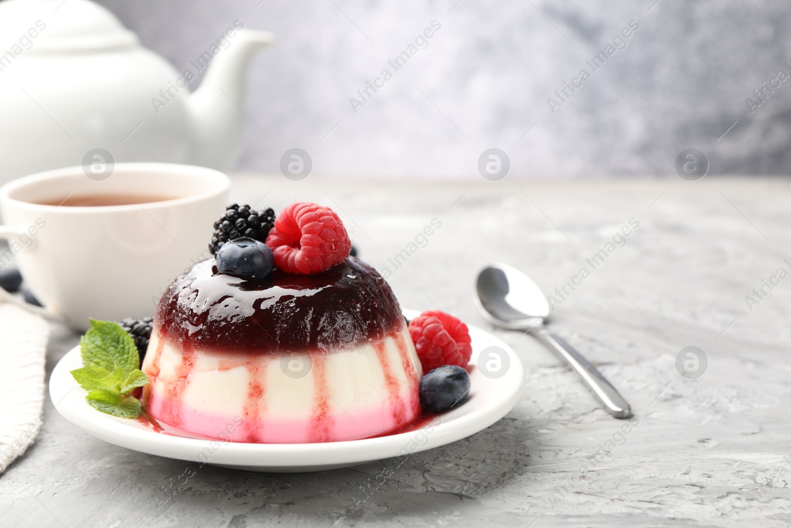 Photo of Tasty panna cotta with berries and jam on light grey table, closeup. Space for text