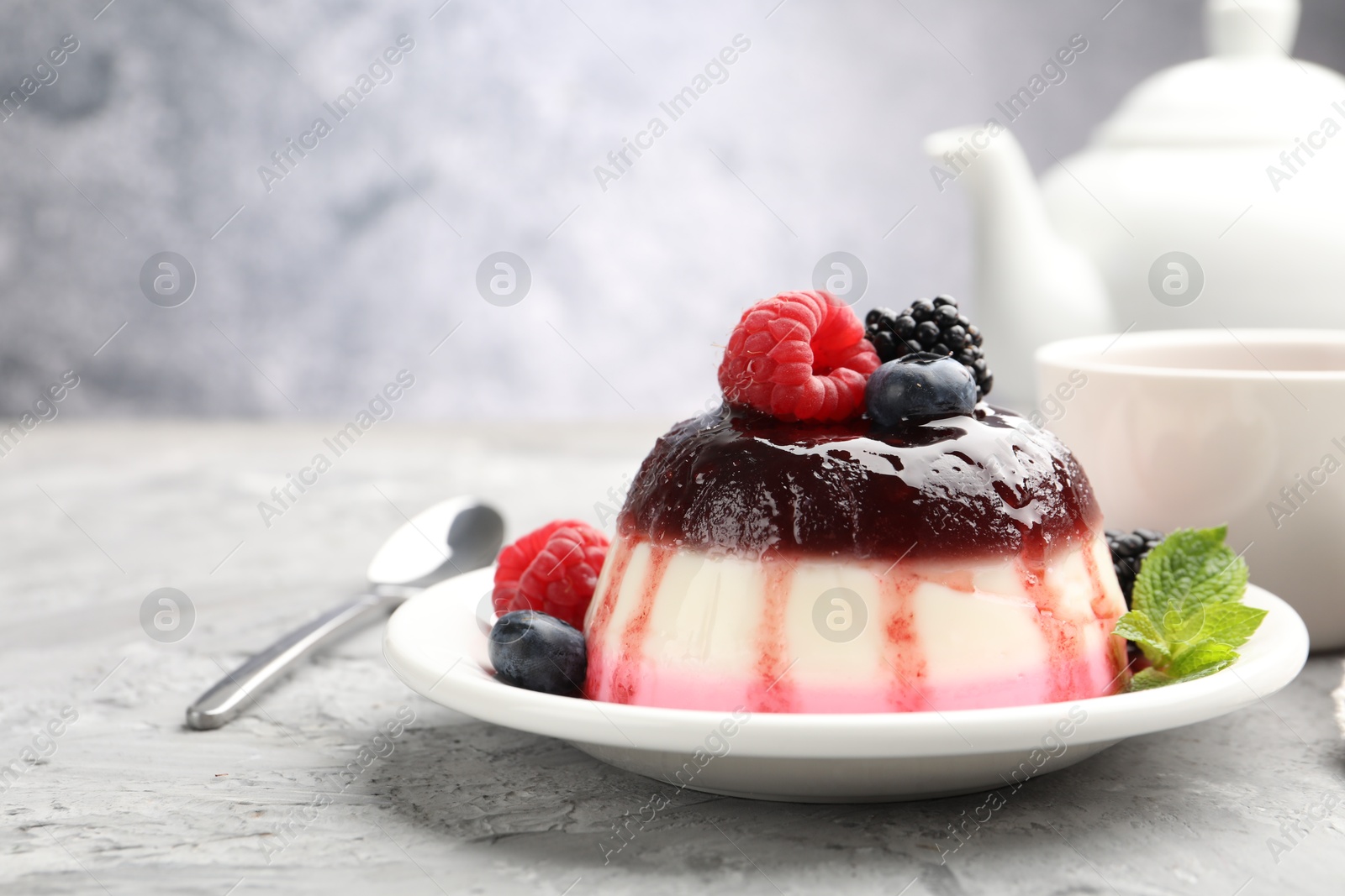 Photo of Tasty panna cotta with berries and jam on light grey table, closeup