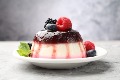 Photo of Tasty panna cotta with berries and jam on light grey table, closeup