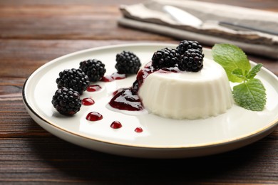 Photo of Tasty panna cotta with blackberries, mint and sauce on wooden table, closeup