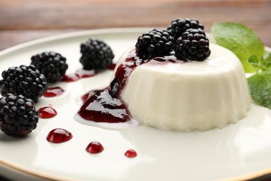 Photo of Tasty panna cotta with blackberries, mint and sauce on table, closeup