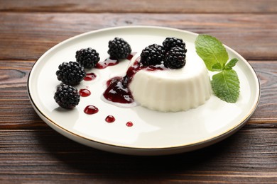 Photo of Tasty panna cotta with blackberries, mint and sauce on wooden table, closeup