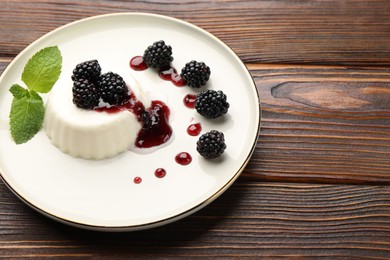 Photo of Tasty panna cotta with blackberries, mint and sauce on wooden table, closeup. Space for text