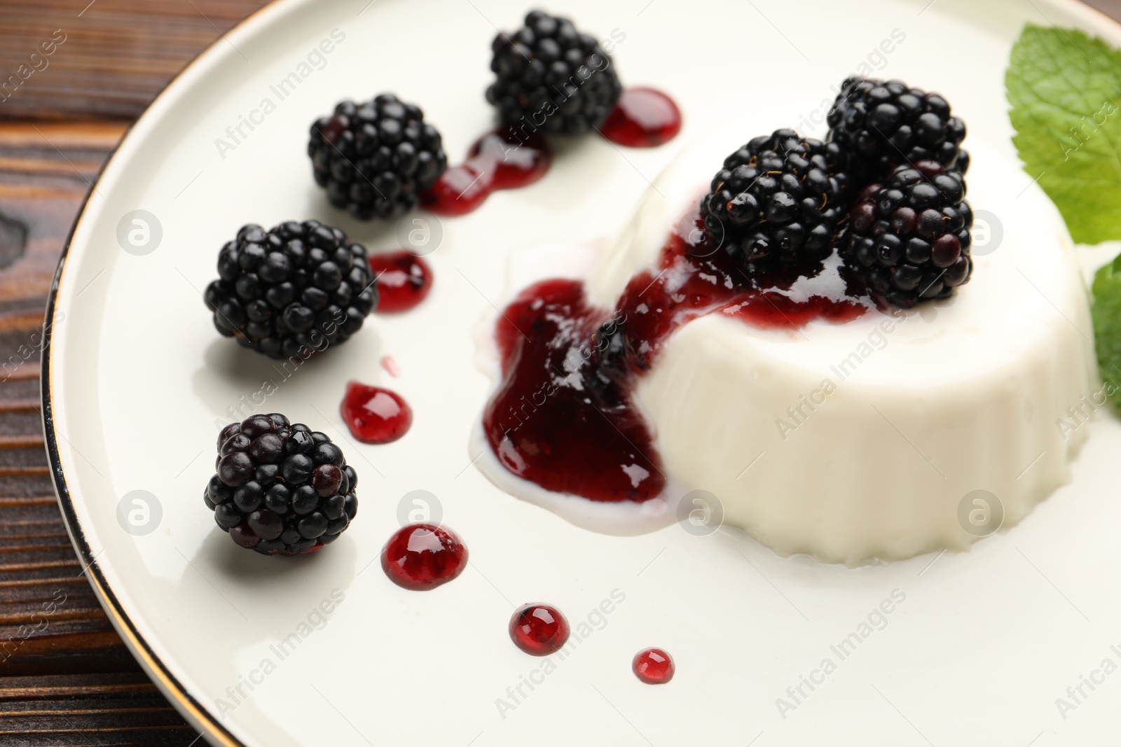 Tasty panna cotta with blackberries, mint and sauce on wooden table, closeup Photo of Tasty panna cotta with blackberries, mint and sauce on wooden table, closeup