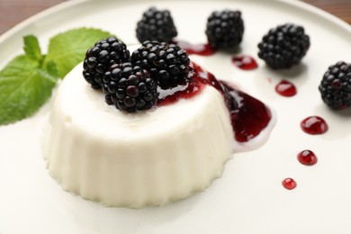 Photo of Tasty panna cotta with blackberries, mint and sauce on table, closeup