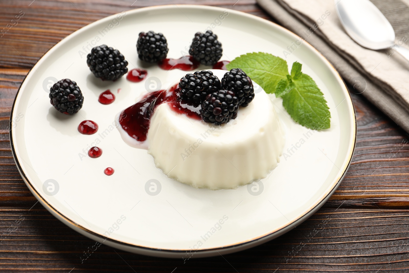 Photo of Tasty panna cotta with blackberries, mint and sauce on wooden table, closeup