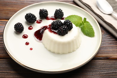 Photo of Tasty panna cotta with blackberries, mint and sauce on wooden table, closeup