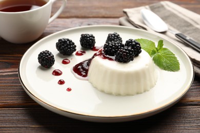 Photo of Tasty panna cotta with blackberries, mint and sauce on wooden table, closeup