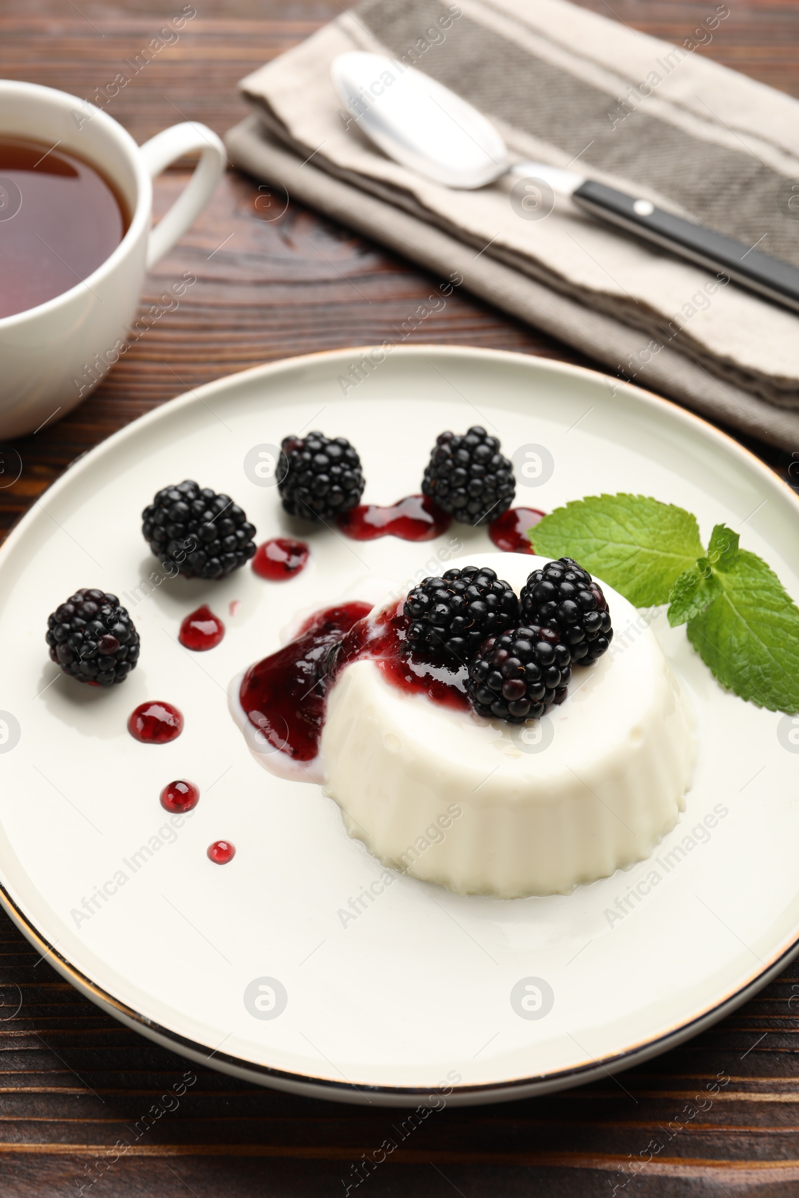 Photo of Tasty panna cotta with blackberries, mint and sauce on wooden table, closeup