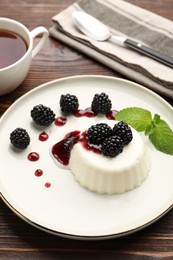 Photo of Tasty panna cotta with blackberries, mint and sauce on wooden table, closeup