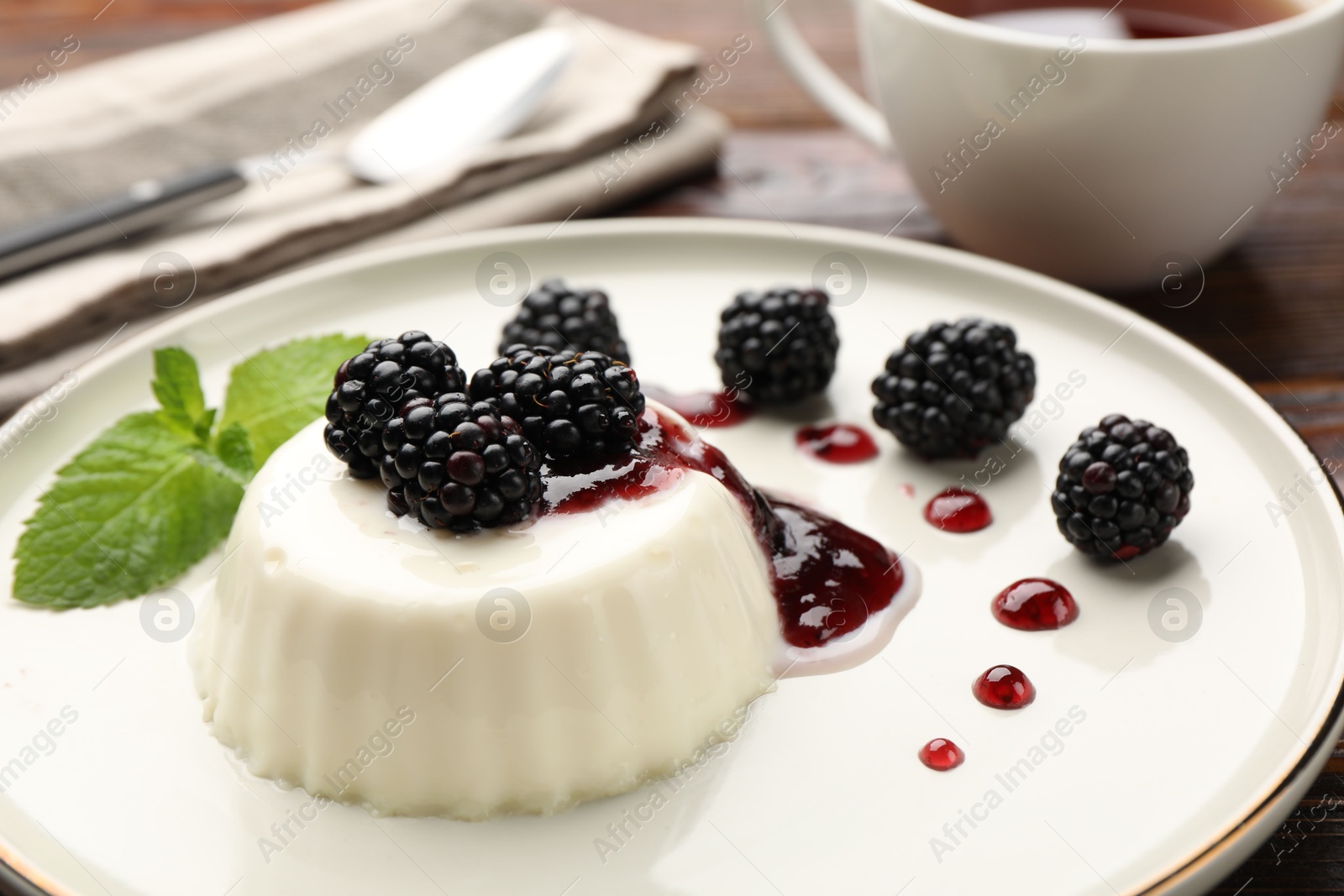 Tasty panna cotta with blackberries, mint and sauce on wooden table, closeup Photo of Tasty panna cotta with blackberries, mint and sauce on wooden table, closeup