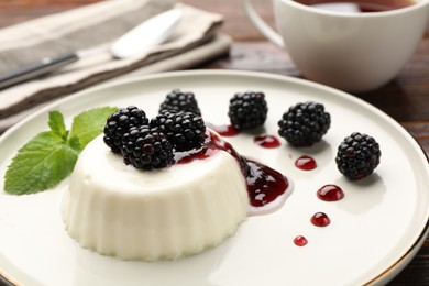 Photo of Tasty panna cotta with blackberries, mint and sauce on wooden table, closeup