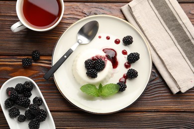 Photo of Tasty panna cotta with blackberries, mint and sauce on wooden table, flat lay