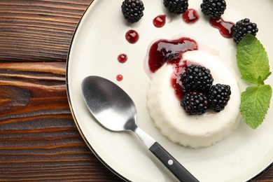 Photo of Tasty panna cotta with blackberries, mint and sauce on wooden table, top view
