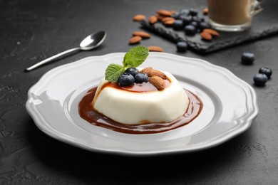 Photo of Tasty panna cotta with blueberries, almonds and sauce on black table, closeup