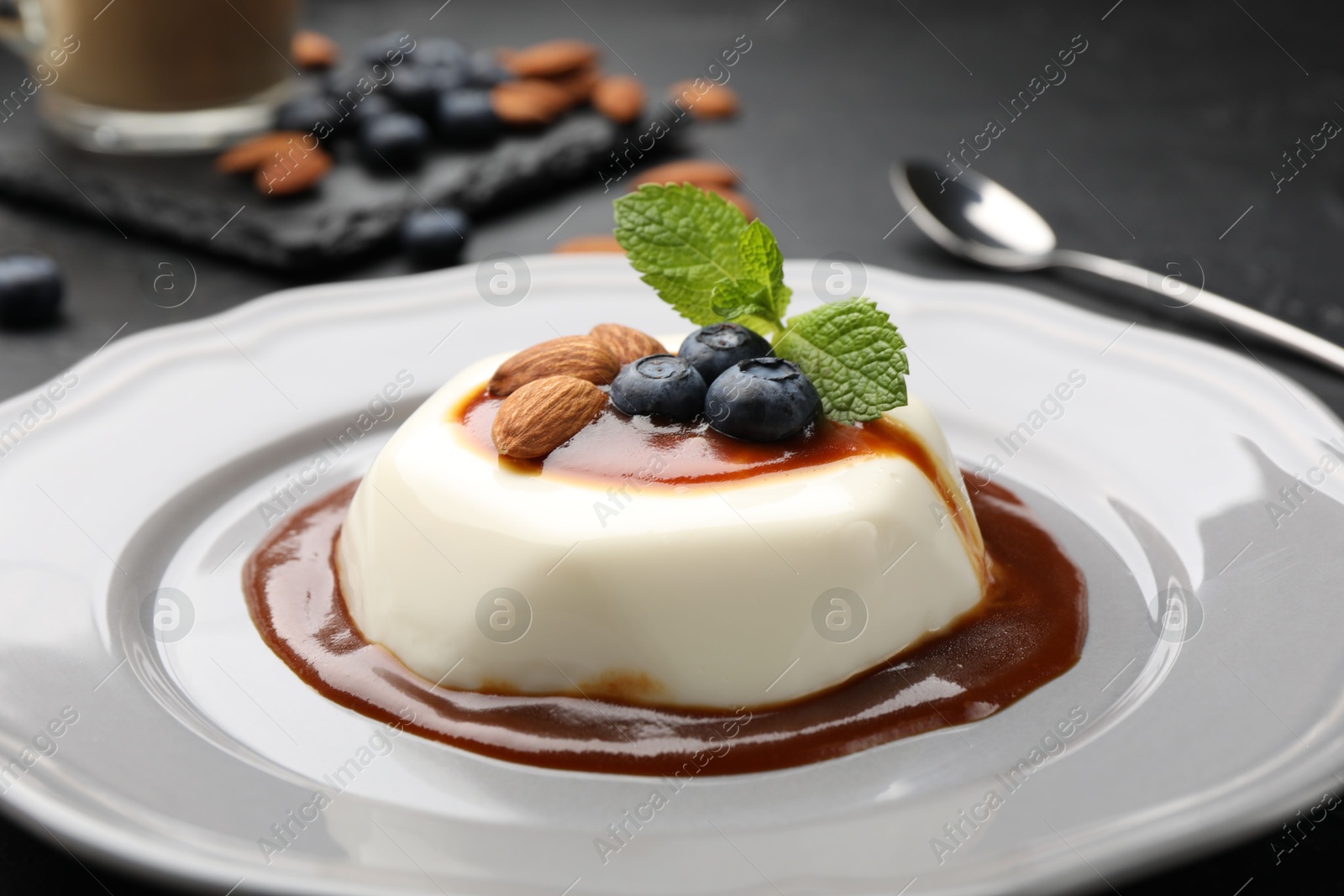 Photo of Tasty panna cotta with blueberries, almonds and sauce on black table, closeup