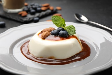 Photo of Tasty panna cotta with blueberries, almonds and sauce on black table, closeup