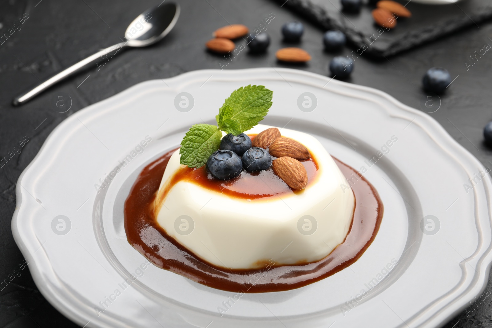 Photo of Tasty panna cotta with blueberries, almonds and sauce on black table, closeup