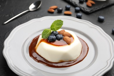 Photo of Tasty panna cotta with blueberries, almonds and sauce on black table, closeup