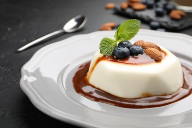 Photo of Tasty panna cotta with blueberries, almonds and sauce on black table, closeup