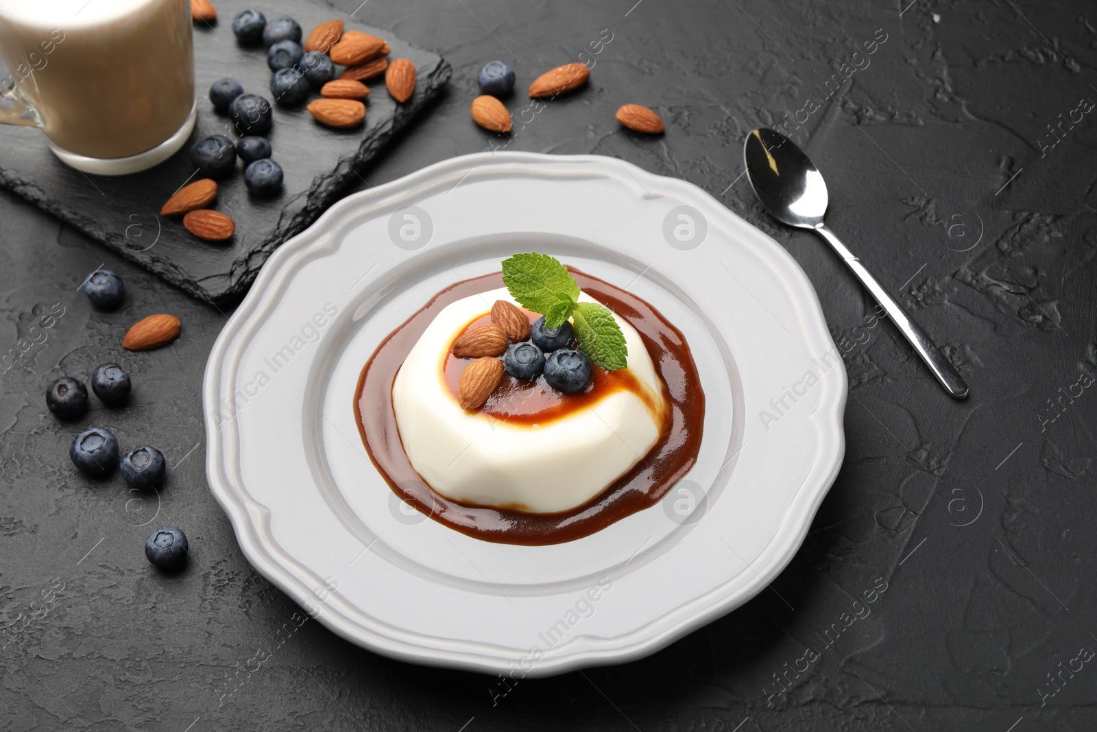 Photo of Tasty panna cotta with blueberries, almonds and sauce on black table, closeup
