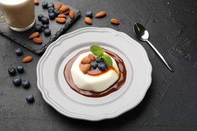 Photo of Tasty panna cotta with blueberries, almonds and sauce on black table, closeup