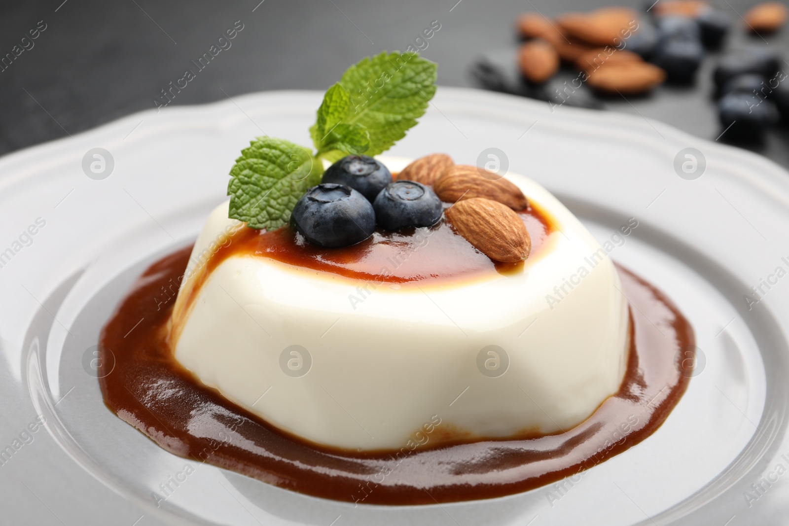Photo of Tasty panna cotta with blueberries, almonds and sauce on black table, closeup