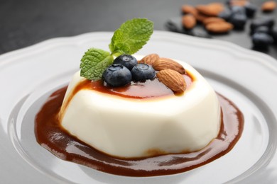 Photo of Tasty panna cotta with blueberries, almonds and sauce on black table, closeup