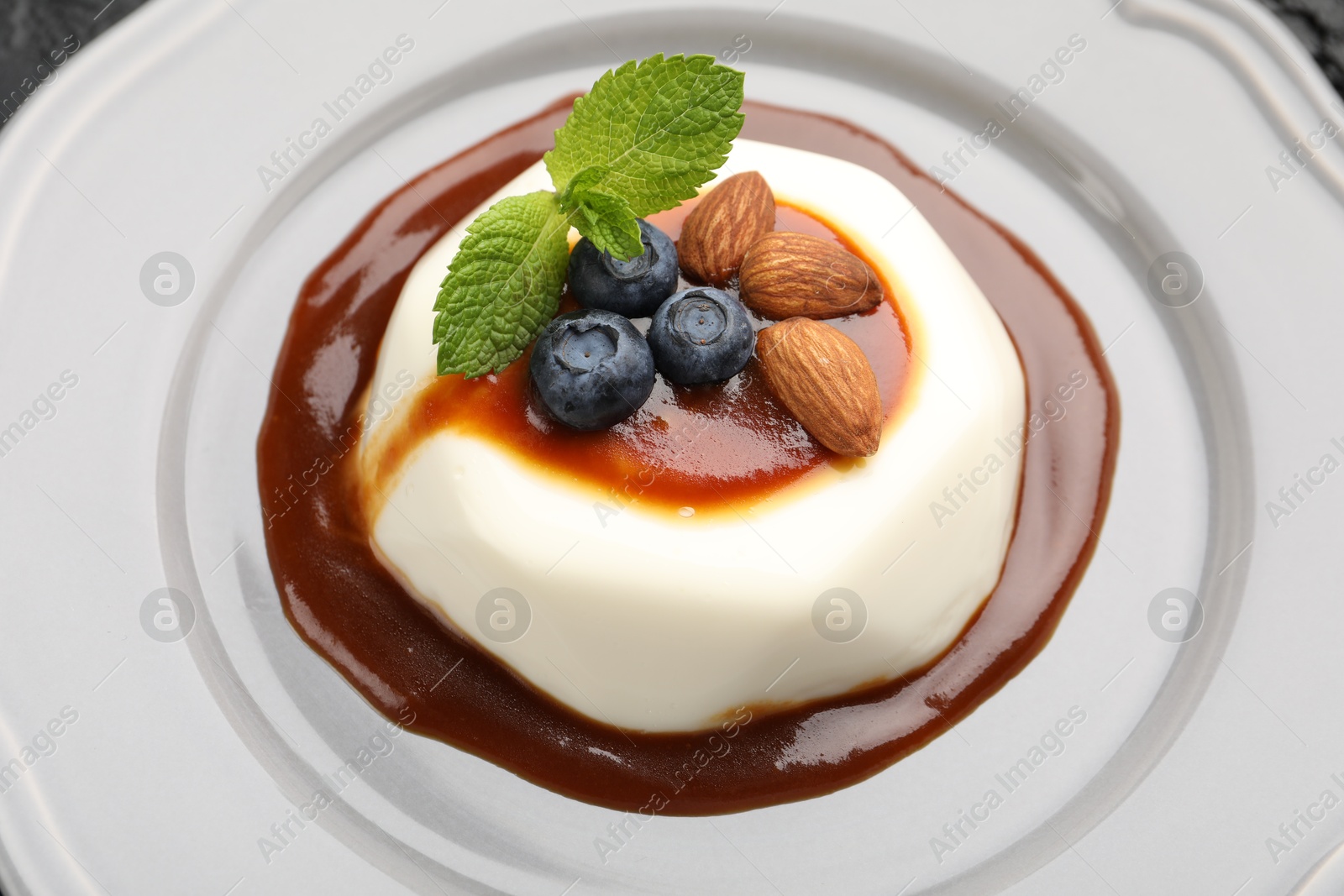 Photo of Tasty panna cotta with blueberries, almonds and sauce on plate, closeup