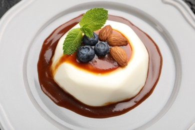 Photo of Tasty panna cotta with blueberries, almonds and sauce on plate, closeup