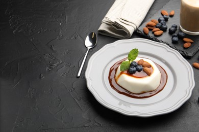 Photo of Tasty panna cotta with blueberries, almonds and sauce on black table, closeup. Space for text