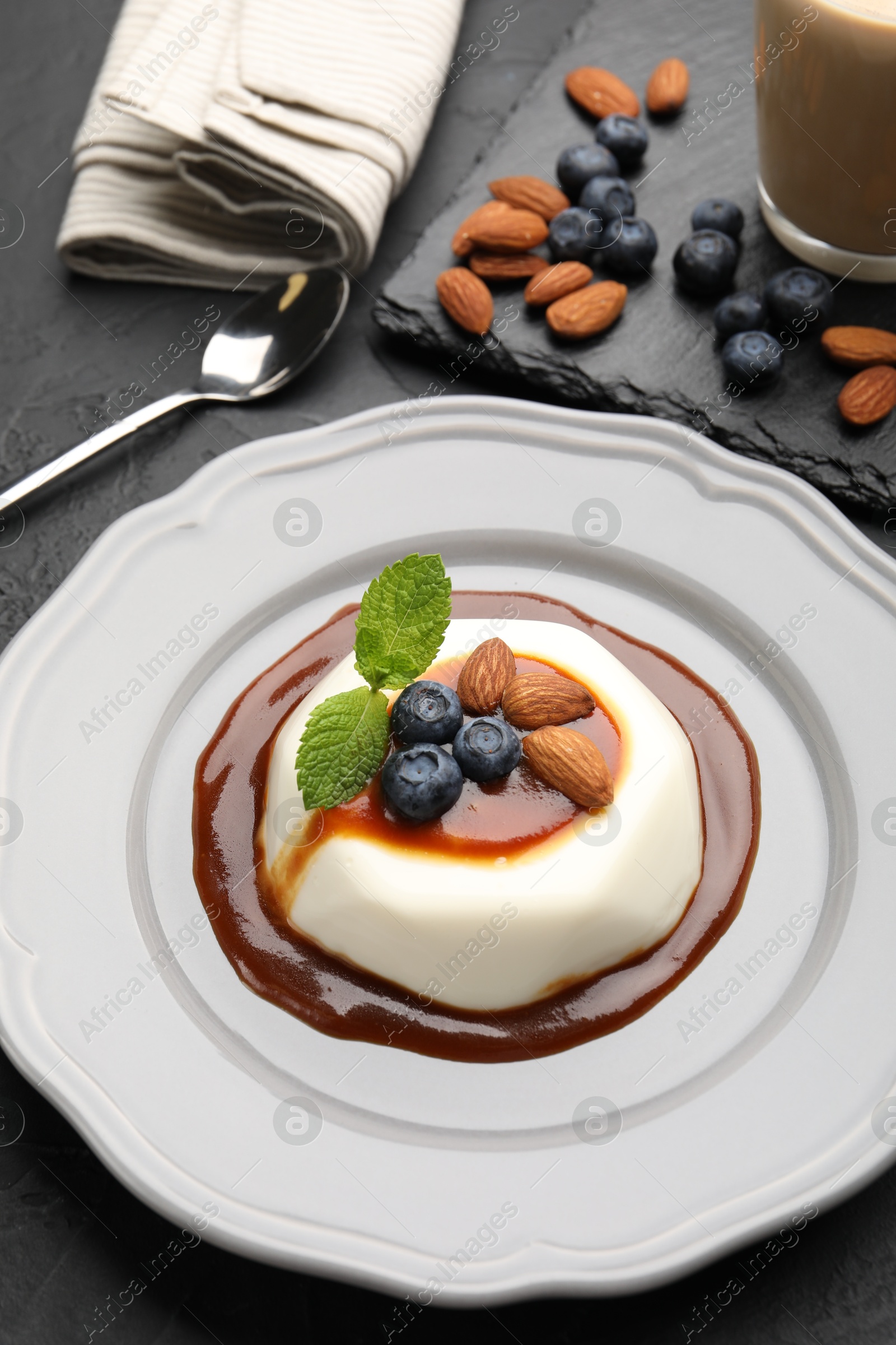 Photo of Tasty panna cotta with blueberries, almonds and sauce on black table, closeup