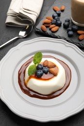 Photo of Tasty panna cotta with blueberries, almonds and sauce on black table, closeup