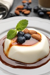 Photo of Tasty panna cotta with blueberries, almonds and sauce on table, closeup