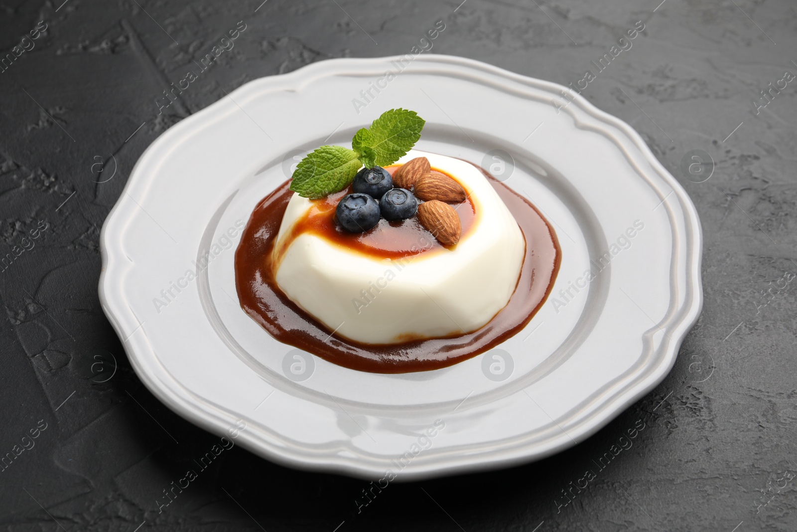 Photo of Tasty panna cotta with blueberries, almonds and sauce on black table, closeup