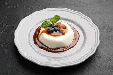 Photo of Tasty panna cotta with blueberries, almonds and sauce on black table, closeup