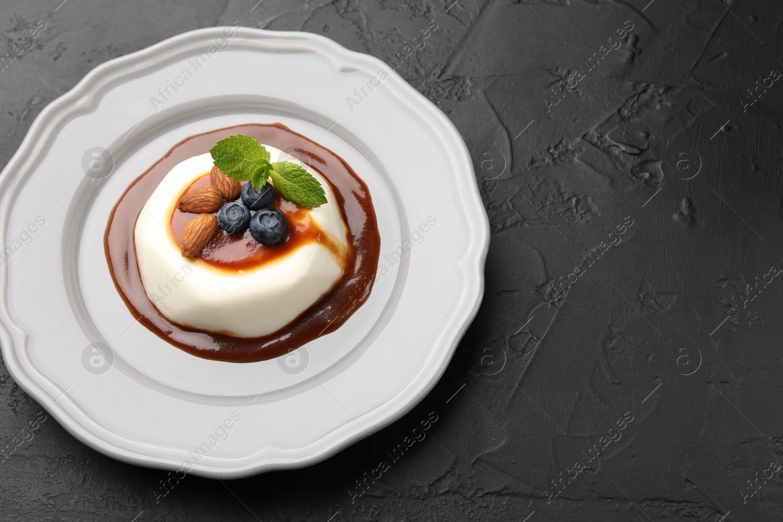 Photo of Tasty panna cotta with blueberries, almonds and sauce on black table, closeup. Space for text