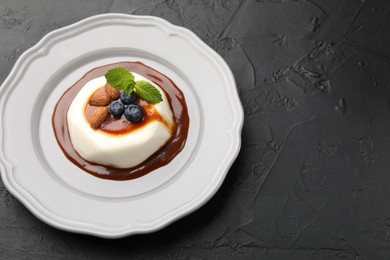 Photo of Tasty panna cotta with blueberries, almonds and sauce on black table, closeup. Space for text