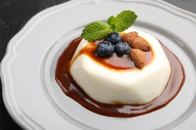 Photo of Tasty panna cotta with blueberries, almonds and sauce on black table, closeup