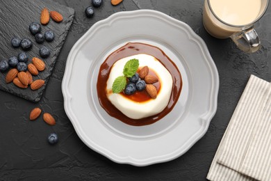 Photo of Tasty panna cotta with blueberries, almonds and sauce on black table, flat lay