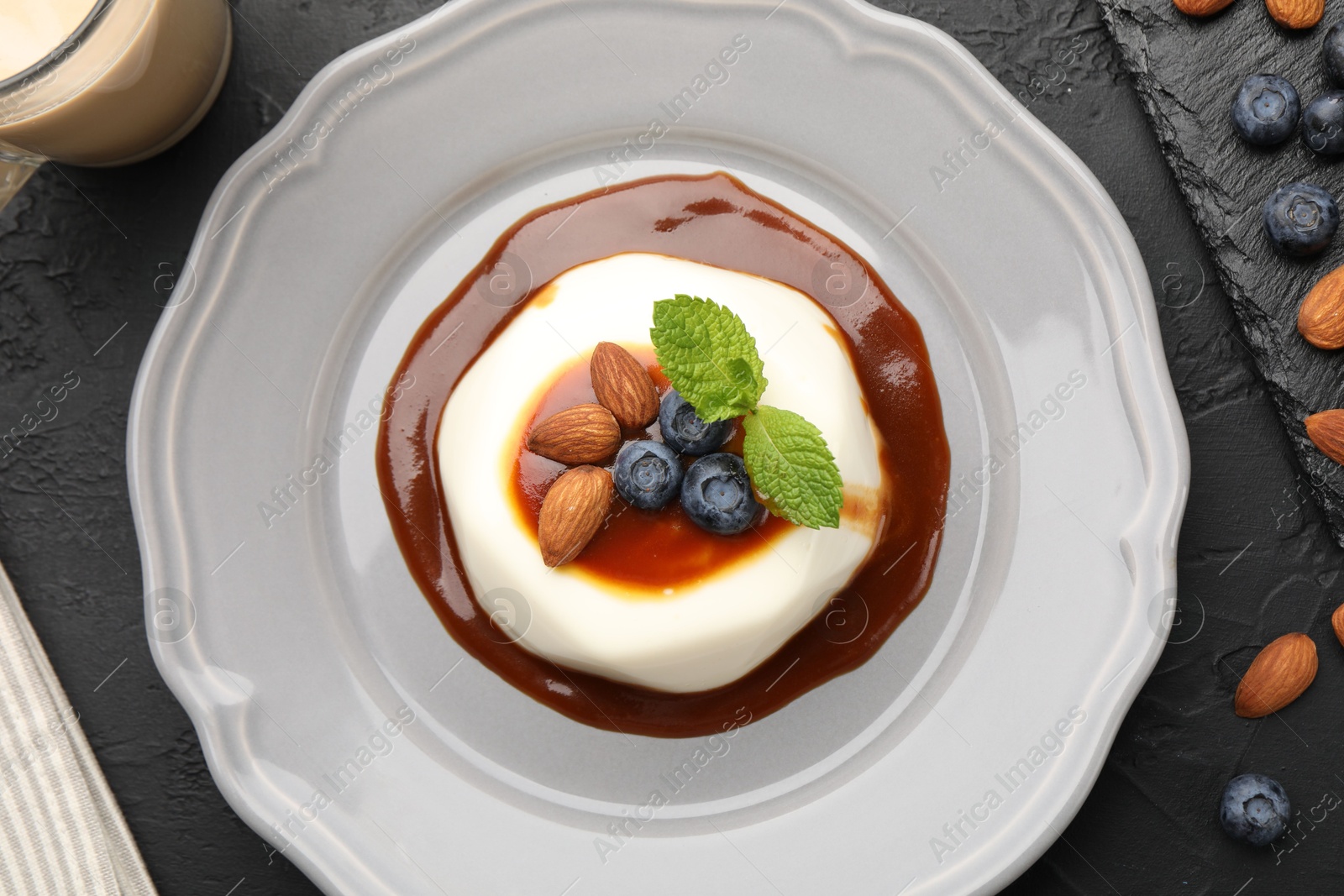 Photo of Tasty panna cotta with blueberries, almonds and sauce on black table, flat lay
