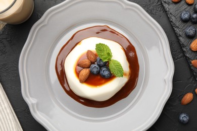 Photo of Tasty panna cotta with blueberries, almonds and sauce on black table, flat lay