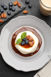 Photo of Tasty panna cotta with blueberries, almonds and sauce on black table, flat lay