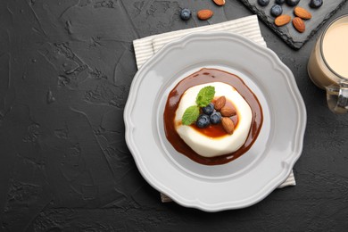 Photo of Tasty panna cotta with blueberries, almonds and sauce on black table, flat lay. Space for text