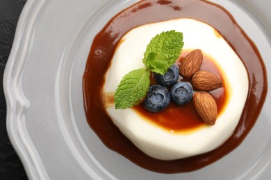 Photo of Tasty panna cotta with blueberries, almonds and sauce on black table, top view