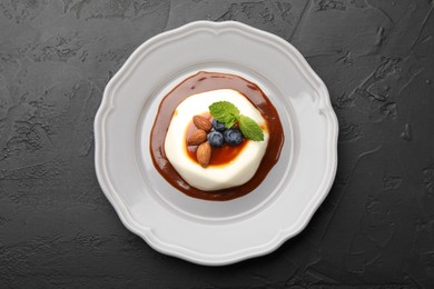 Photo of Tasty panna cotta with blueberries, almonds and sauce on black table, top view