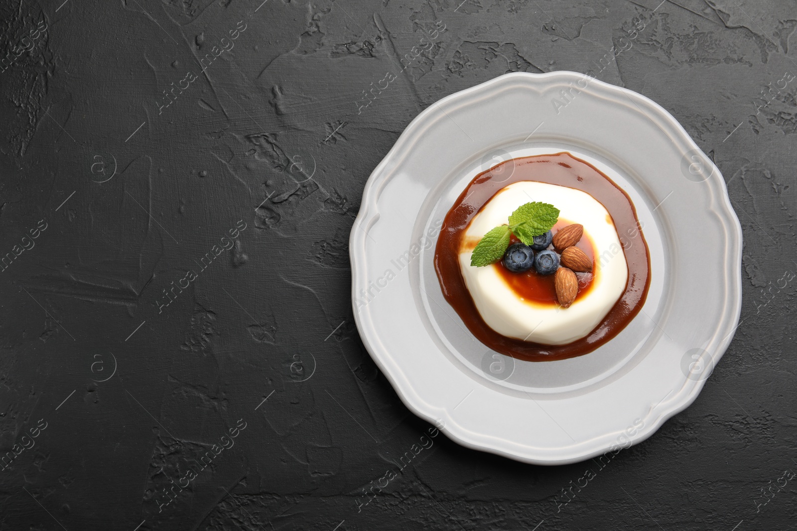 Photo of Tasty panna cotta with blueberries, almonds and sauce on black table, top view. Space for text