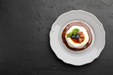 Photo of Tasty panna cotta with blueberries, almonds and sauce on black table, top view. Space for text