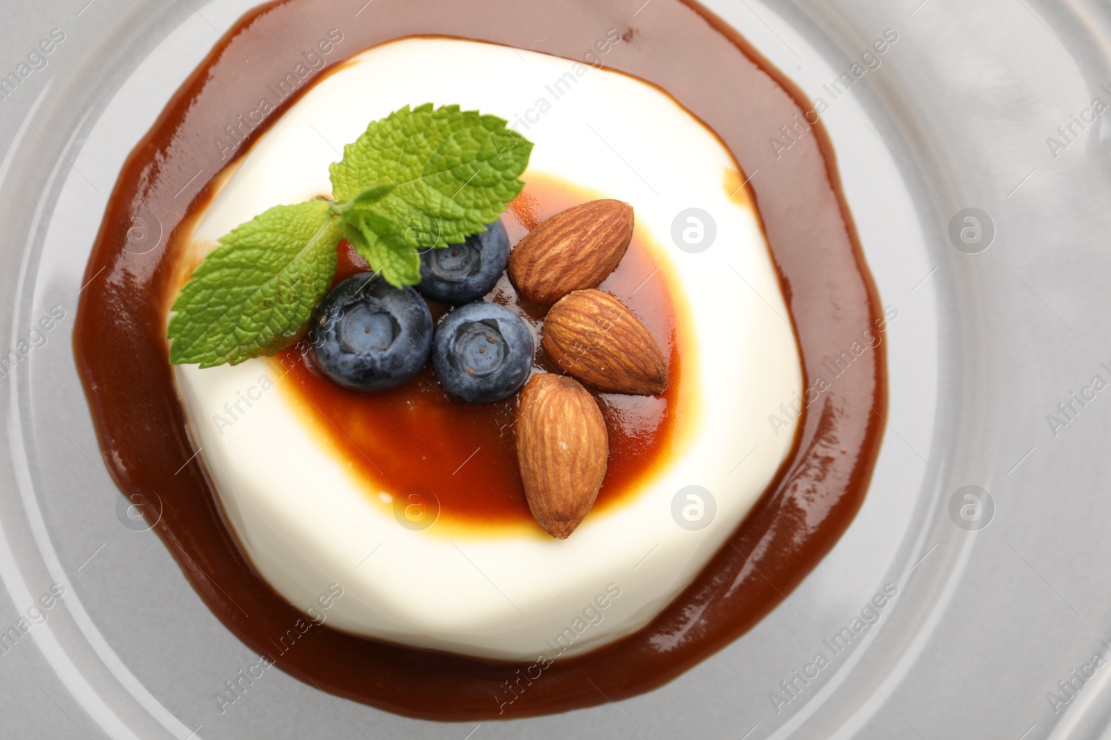 Photo of Tasty panna cotta with blueberries, almonds and sauce on plate, top view