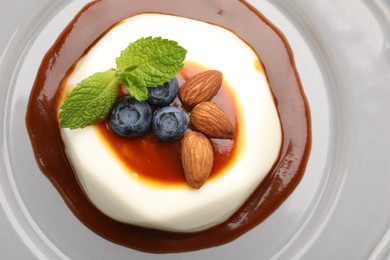 Photo of Tasty panna cotta with blueberries, almonds and sauce on plate, top view